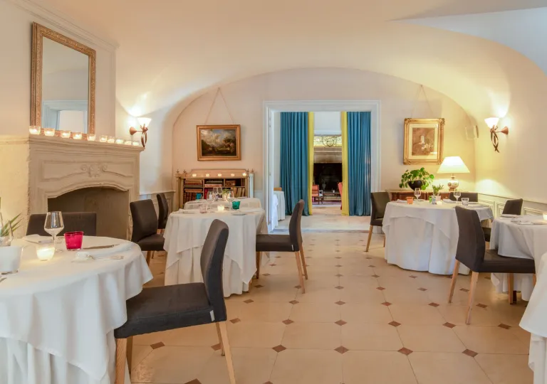 The dining room at Manoir d'Hautegente features arched ceilings, terracotta tiled floors, and dark upholstered chairs with a stone fireplace.