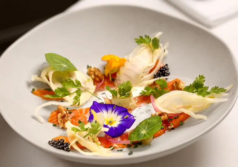 A fine-dining dish features cured salmon served with fennel, edible flowers, walnuts, and caviar.
