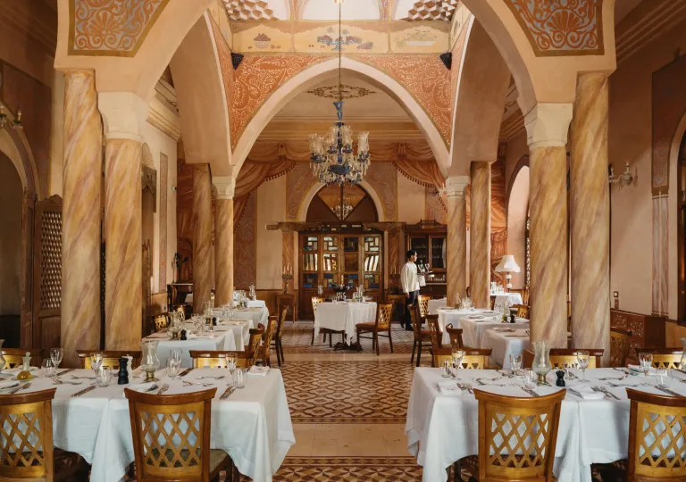 Le Great Room dining room inside the Al Moudira Hotel in Luxor, Egypt features an ornate, palace-like setting featuring hand-painted ceilings and towering marble pillars.