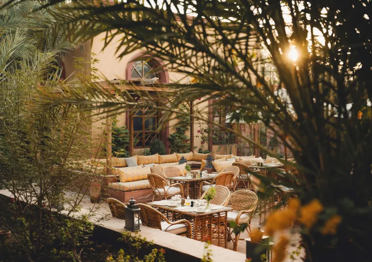 The outdoor courtyard patio restaurant at the Al Moudira Hotel in Luxor, Egypt that features an open-air dining space framed by lush gardens and palm trees.