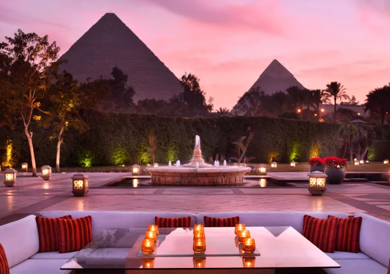 Sunset view at the outdoor lounge area at the historic Marriott Mena House, Cairo in Giza, Egypt with the Great Pyramids looming directly behind the manicured hedges.