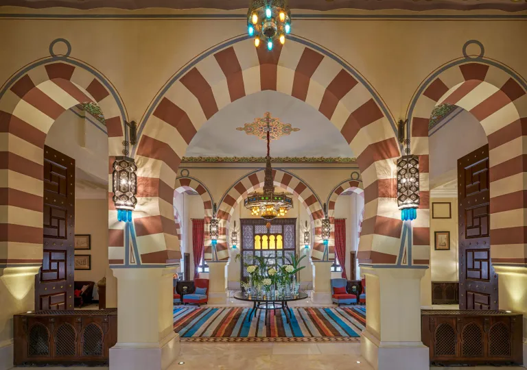 Moorish-style lobby of the Old Cataract Aswan hotel in Egypt featuring striking striped horseshoe arches, intricate hanging lanterns, and traditional geometric plasterwork.