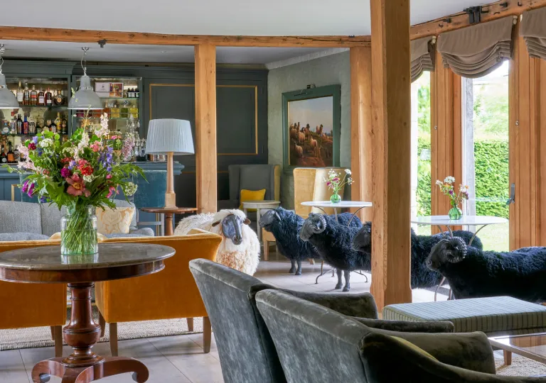 The Baa Bar inside the Thyme hotel and estate in Southrop, Cotswolds, England featuring velvet chairs and lifelike black and white sheep statues.