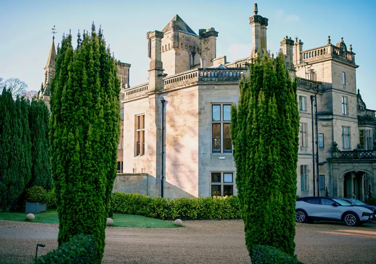 Exterior view of castle-like building with large trees and a dirt road in front