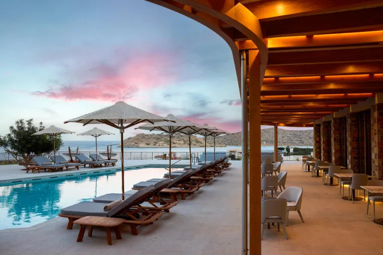 A hotel pool with many lounge chairs overlooks the Mediterranean sea.