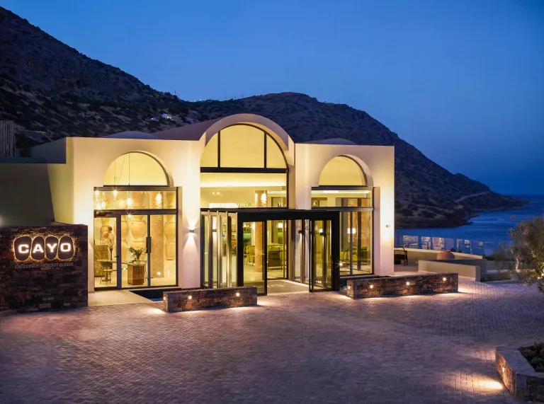Night view of Cayo resort entrance with hills and ocean in the background.