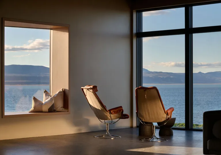 Two mid-century modern leather and canvas lounge chairs overlooking a scenic view of the water at the Black Sand Hotel in  Ölfus, Iceland.