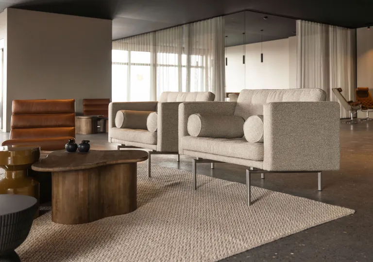 Mid-century style lounge seating featuring upholstered neutral fabric armchairs, leather chairs and organic shaped wood coffee tables at the Black Sand Hotel in Ölfus, Iceland.