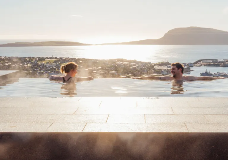Man and woman relaxing in a large pool, with a lake in the background