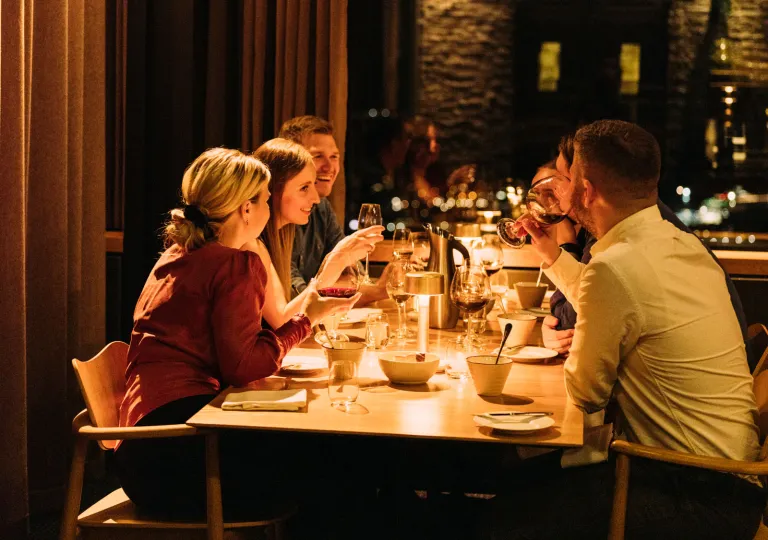 Group of people sitting at a dining table, holding glasses of wine and smiling
