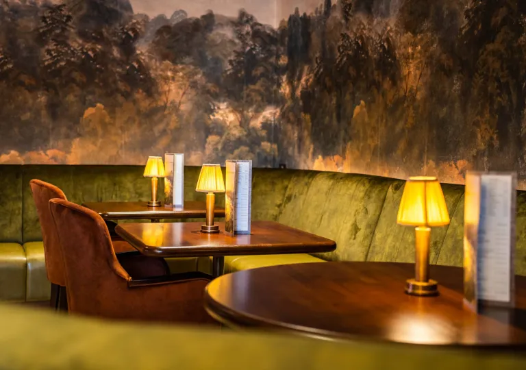 Corner of restaurant with wooden dining tables and velvet chairs