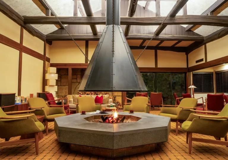Lounge area at Ochiairo Hotel in Japan featuring a large central hearth with an open fire, wood-beam ceilings, comfortable seating arranged in a circle, and warm ambient lighting inspired by traditional Japanese design.