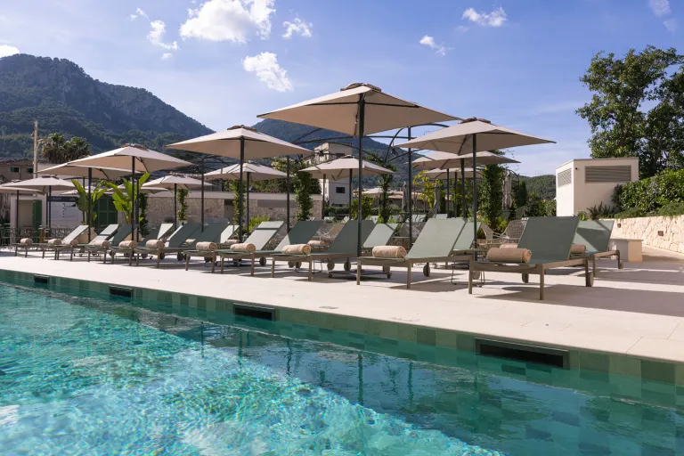 Outdoor pool with reclining chairs and large, beige umbrellas