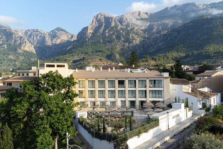 Exterior view of multi-floor hotel building, surrounded by tall trees and mountains in the background