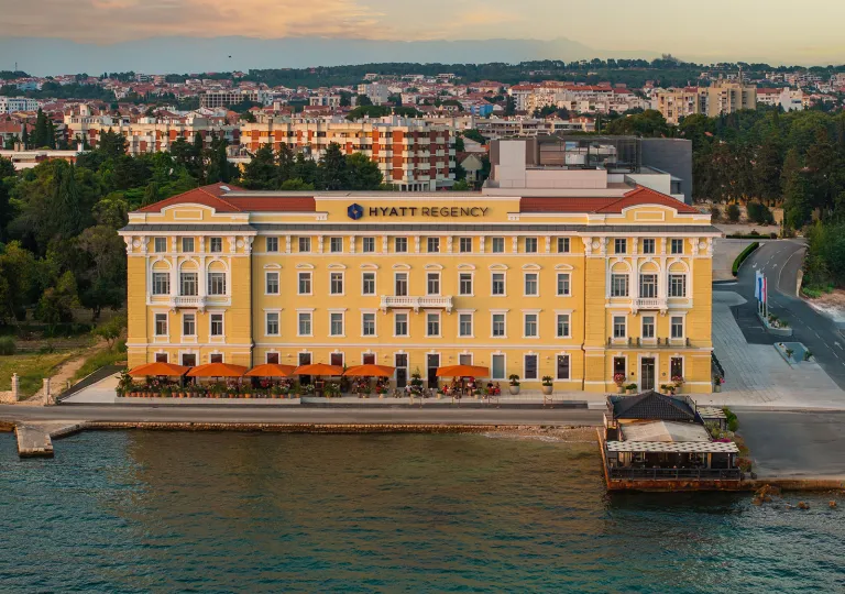 Exterior view of large, yellow and beige hotel building with the ocean in front
