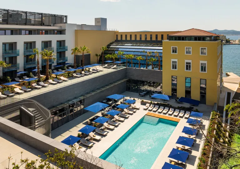 Exterior view of yellow and white hotel building with an outdoor pool and blue chairs