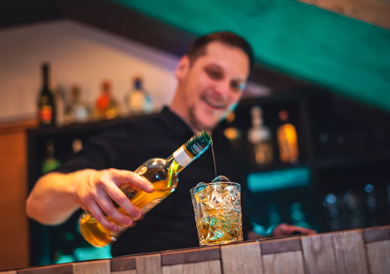 Male bartender pouring alcohol into a glass filled with ice