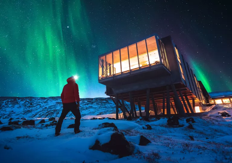 Man walking towards an elevated hotel building, with an aurora in the sky