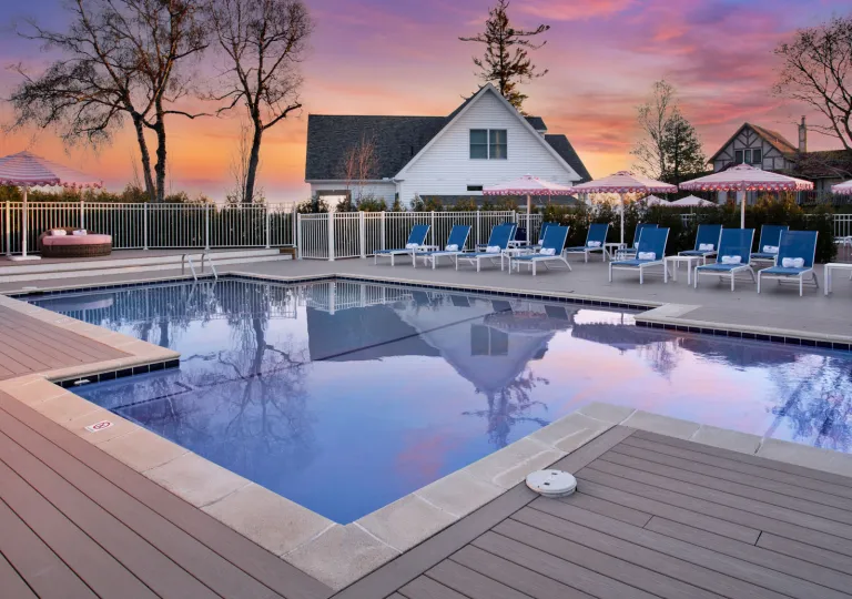 Outdoor pool with the sunset in the background and a large, white house