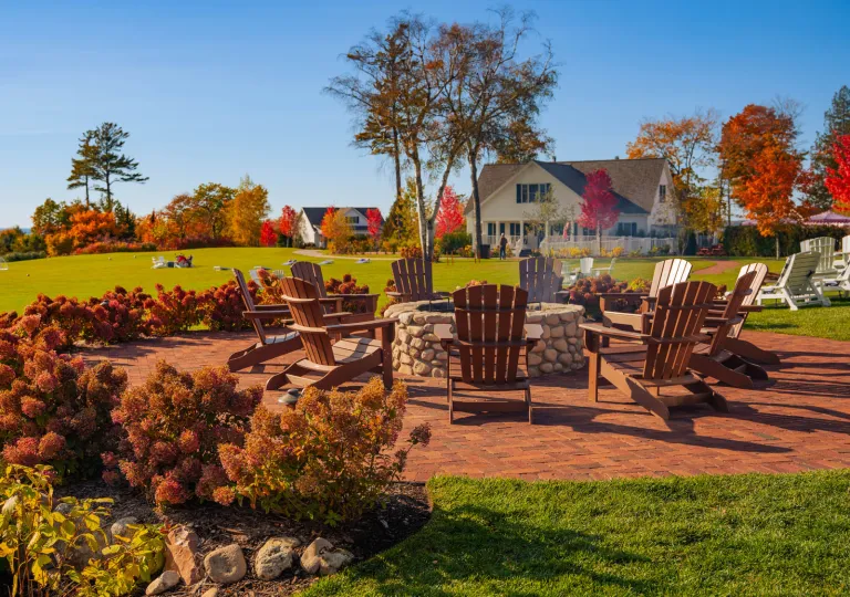 Large lawn area with wooden chairs surrounding a large, stone firepit