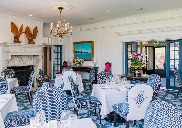 Restaurant with white table cloths over square tables, with blue and white chairs