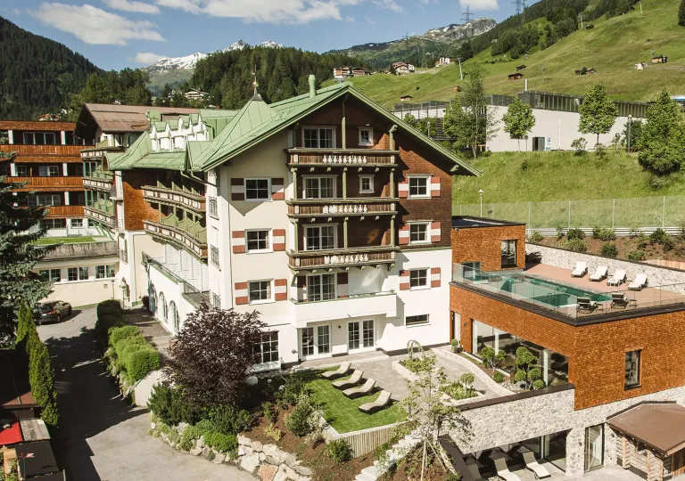 Exterior view of white, brown and green hotel building, with a grassy valley in the background