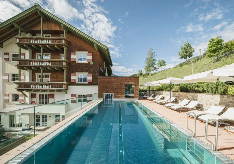 Exterior view of white and brown hotel building with an outdoor pool in front