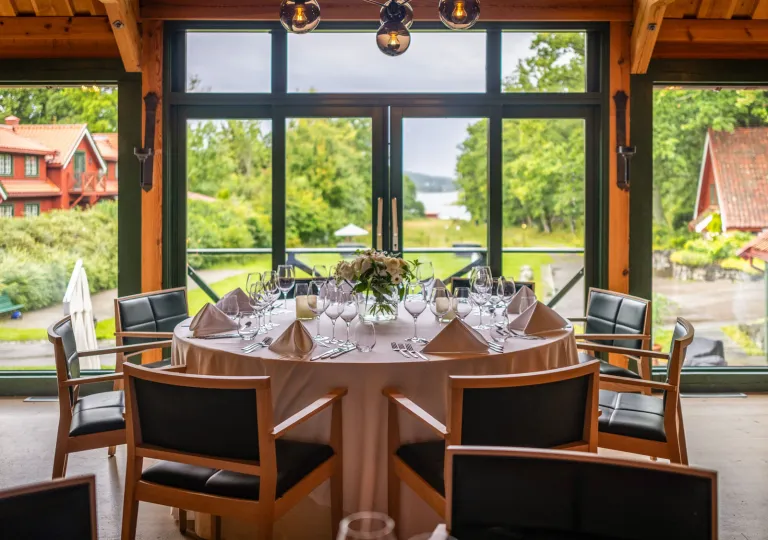 Large, wooden circular table with black cushioned chairs, with a large lawn in the background