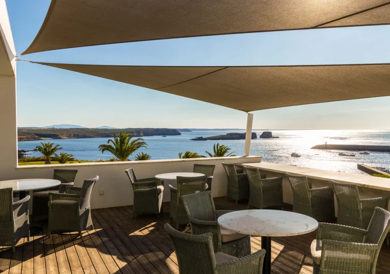 This terrace at the Memmo Baleeira Hotel in Sagres, Portugal, featuring comfortable outdoor seating, tables, and sun sails.