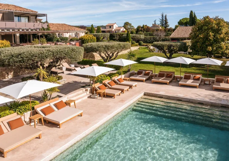 La Bastide Saint Georges hotel in Forcalquier features a tranquil outdoor pool surrounded by pool lounge chairs and olive trees.