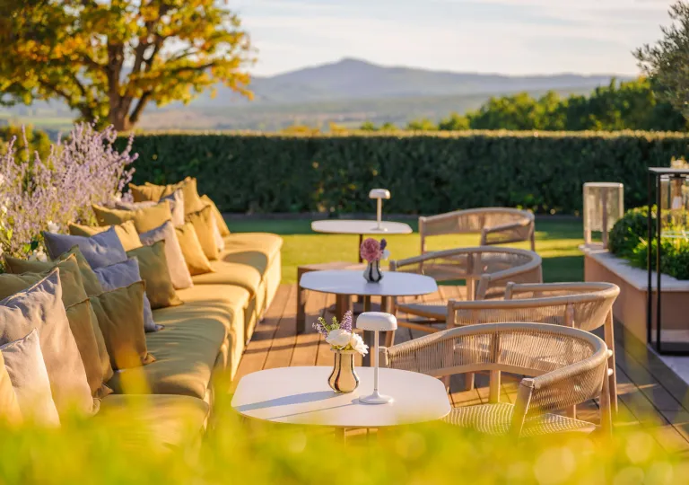 Terrace dining area at Hôtel La Bastide Saint Georges, featuring modern outdoor sofas and woven chairs set against a scenic, hilly landscape.