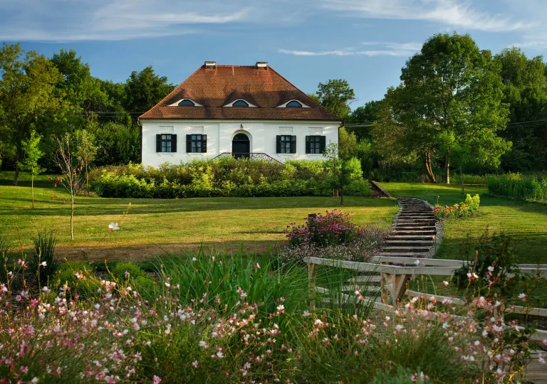 Exterior view of white and red cottage with a garden and grass field in front