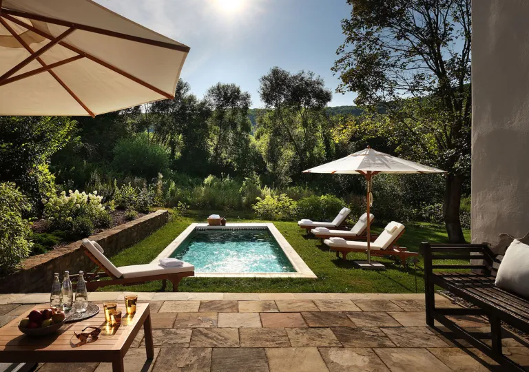 Outdoor pool surrounded by tall trees and white umbrellas
