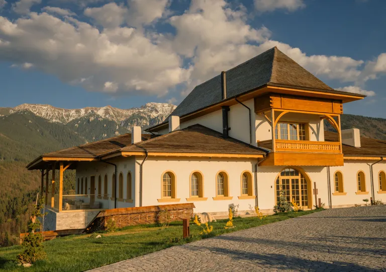 Exterior view of a large white and brown building in a valley, being hit by the sunlight