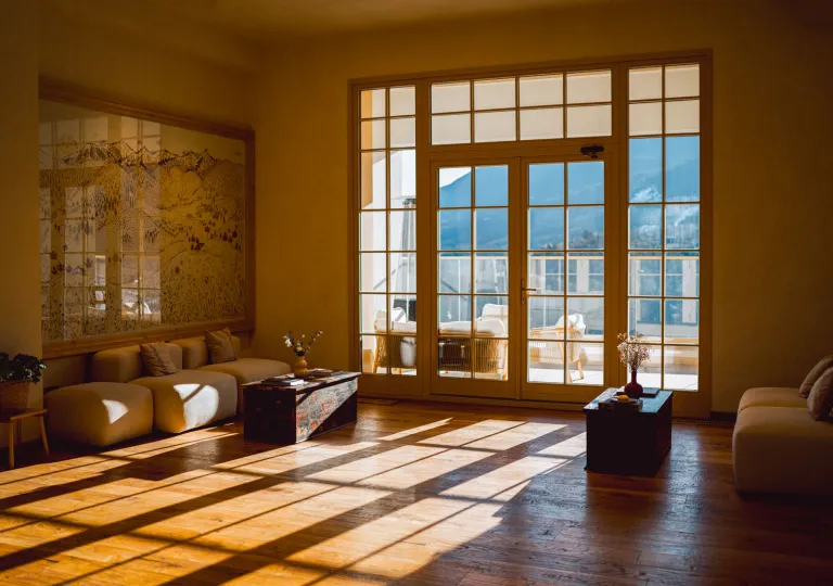 Room with large windows and the sunlight coming through, with large mountains outside