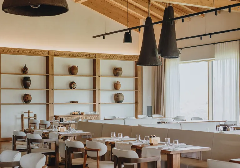 Restaurant dining area with white chairs and tables, with pottery along the walls