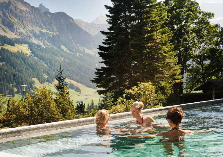 Three people standing in a pool looking out to large mountains