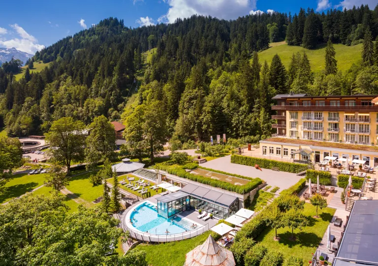 Exterior, sky view of a hotel complex with a garden in front and large hills in the background