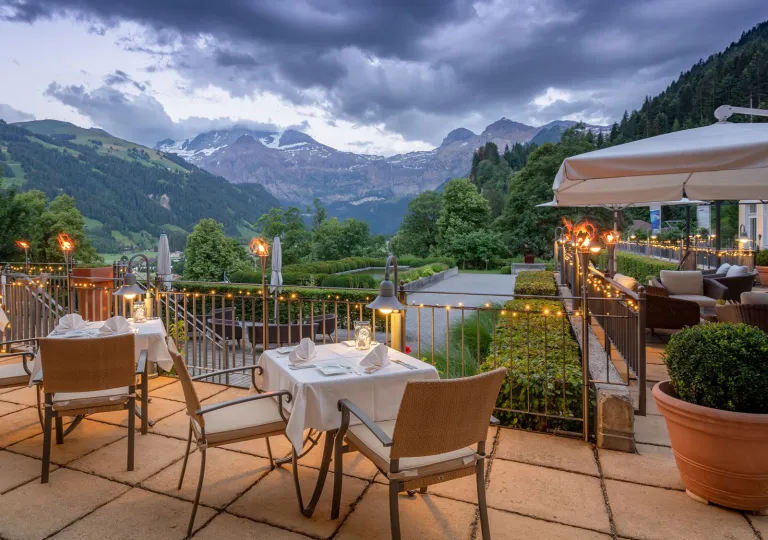 Outdoor patio with dining tables and beige chairs, with mountains in the distance