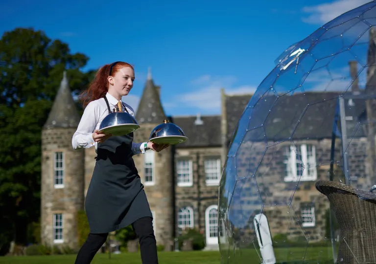 Waitress holding two plates of food walking in front of a castle-styled building