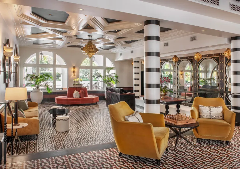 The lobby of the Hotel Californian features Moroccan-inspired geometric ceiling details, yellow velvet chairs, and black-and-white striped columns.