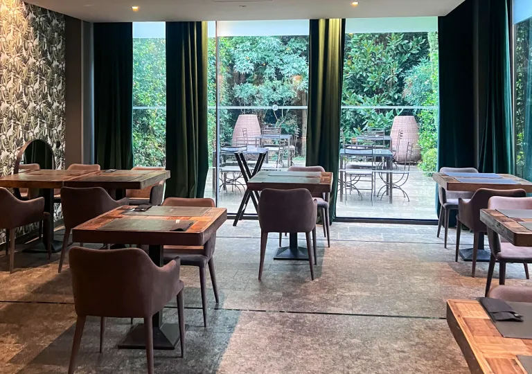 Hotel restaurant with wooden dining tables and chairs, with large windows in the back