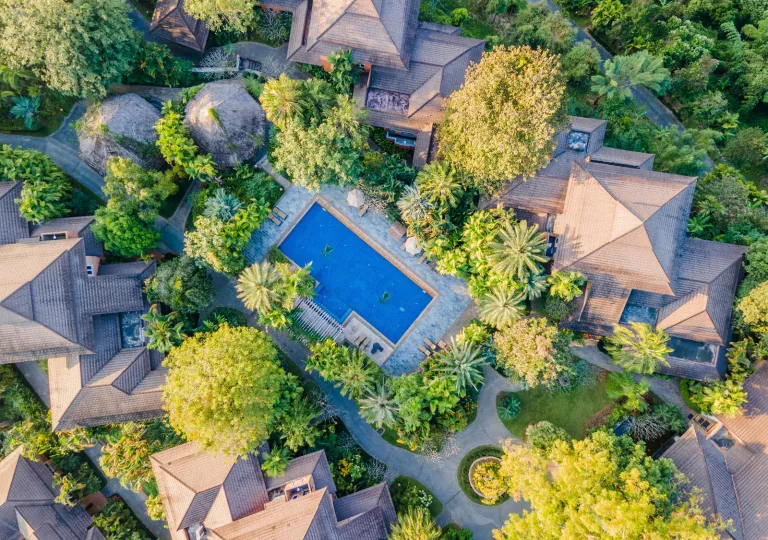 Sky view of beige buildings surrounded trees and an outdoor pool