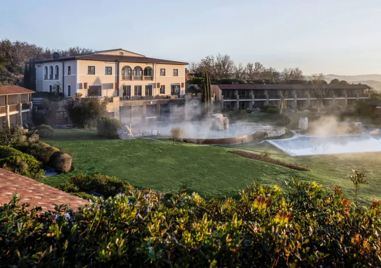 Exterior view of large hotel building with a grass field and outdoor pools in front