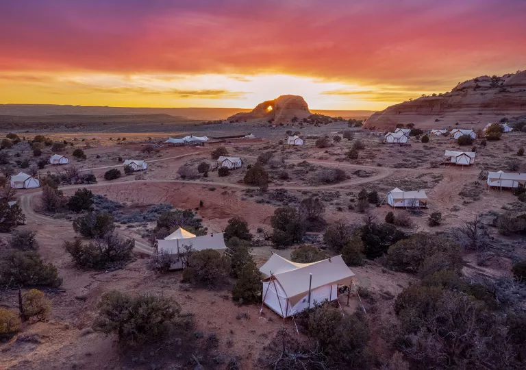 Large tents in a desert, with the sunset in the background