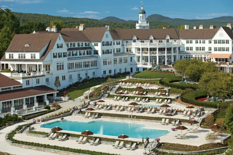 Exterior view of long, white, multi-story hotel building with an outdoor pool in front
