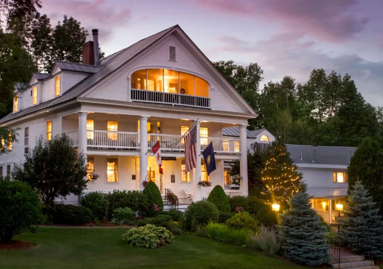 The three-story exterior with grand columns and multi-level wrap-around porches of Rabbit Hill Inn in Lower Waterford, Vermont.