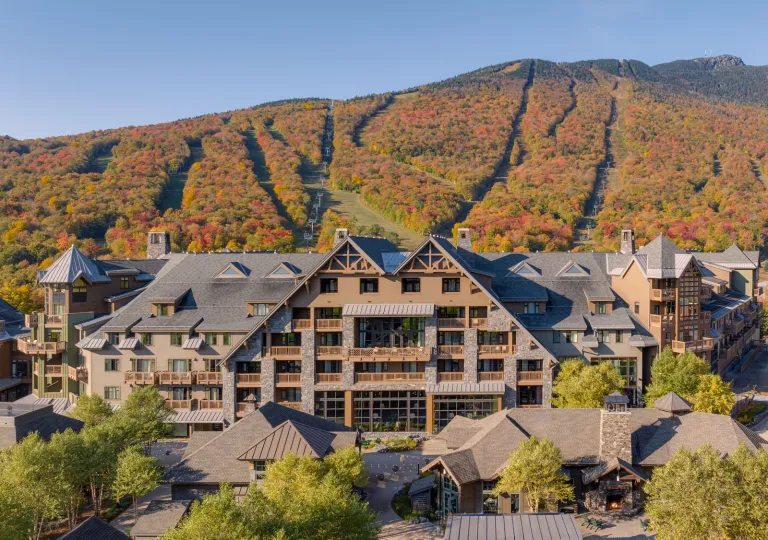 The Lodge at Spruce Peak, a luxury alpine-style resort in Stowe, Vermont, framed by vibrant autumn foliage on the surrounding mountains.