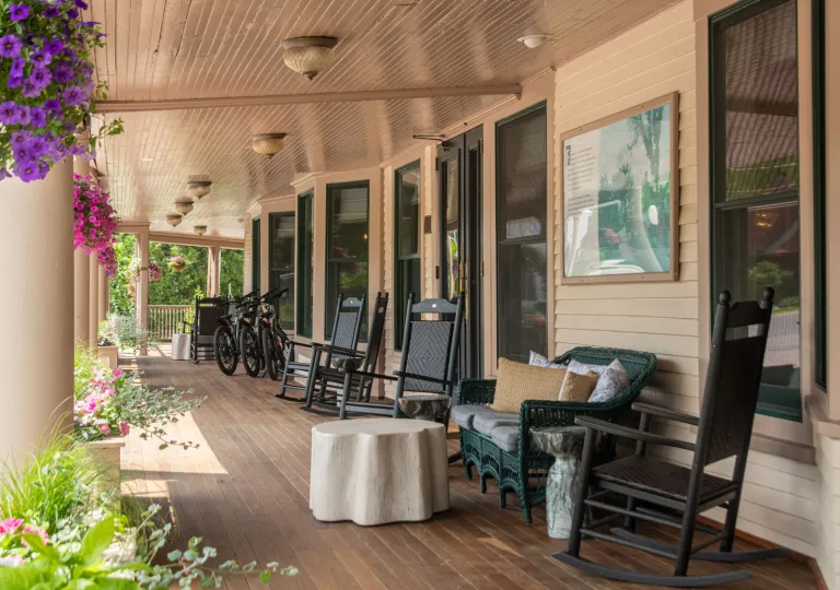 The covered front porch of The Wentworth Inn, featuring rocking chairs, couches and hanging floral baskets