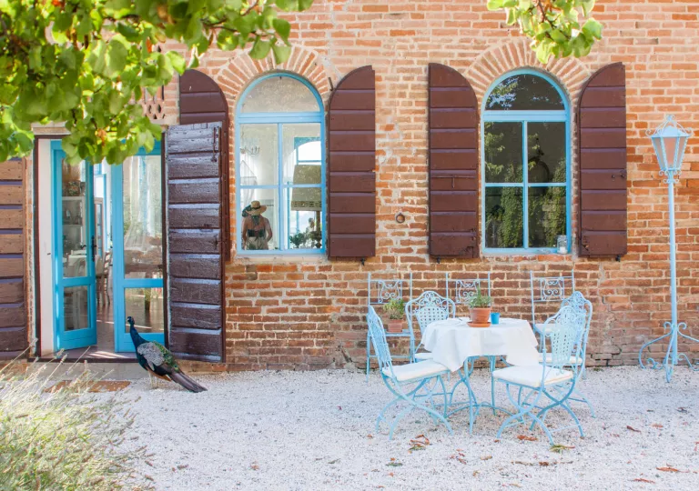 Exterior view of red brick building, with a dining table next to a peacock